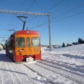Paysage hivernal du Jura avec un train de couleur rouge et orange