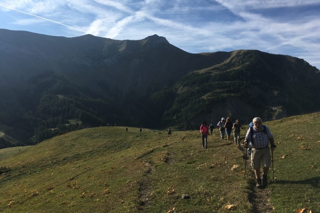 Groupe de randonneurs sur un sentier avec leur guide encadré d'un paysage dans une plaine en montagnes avec des sommets a l'arrière plan