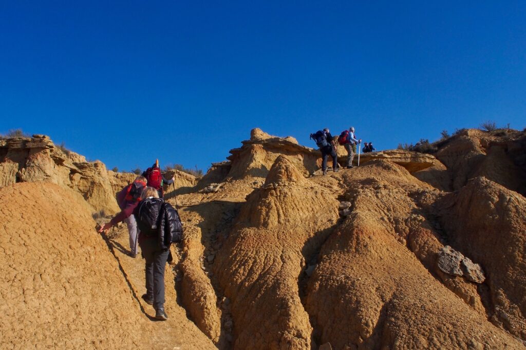 Groupe de randonneurs en train de marcher à flanc des reliefs couleur ocre et sable caractéristiques de la zone des Bardenas