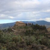 Paysage de montagne avec une habitation au sommet d'une colline encadrée d'arbres et de végétation, dans la zone de Pampelune en Navarre