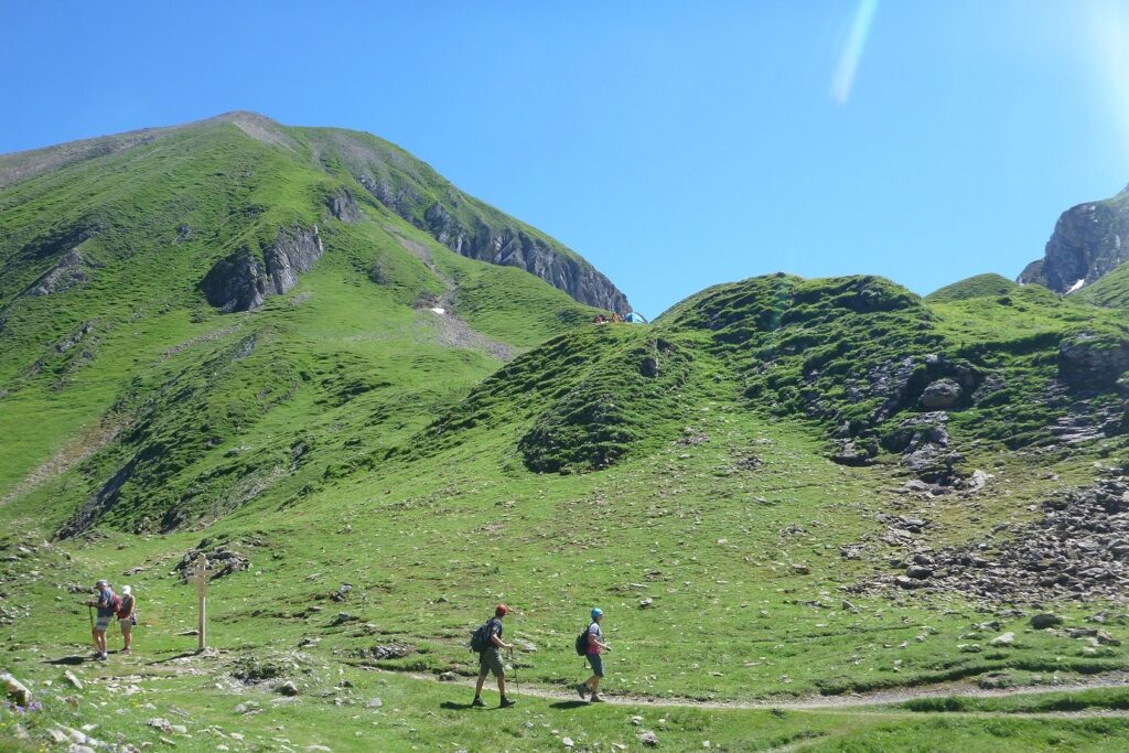 Groupe de randonneurs en liberté sur un sentier de randonnée à travers une plaine avec des sommets couverts d'herbe derrière eux et un paysage estival