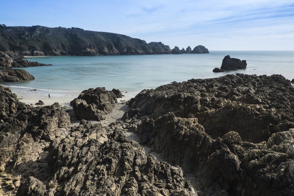 Paysage côtier en Bretagne avec la mer bleu turquoise et des rochers sombres. On aperçoit également le sable de la plage