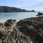 Paysage côtier en Bretagne avec la mer bleu turquoise et des rochers sombres. On aperçoit également le sable de la plage
