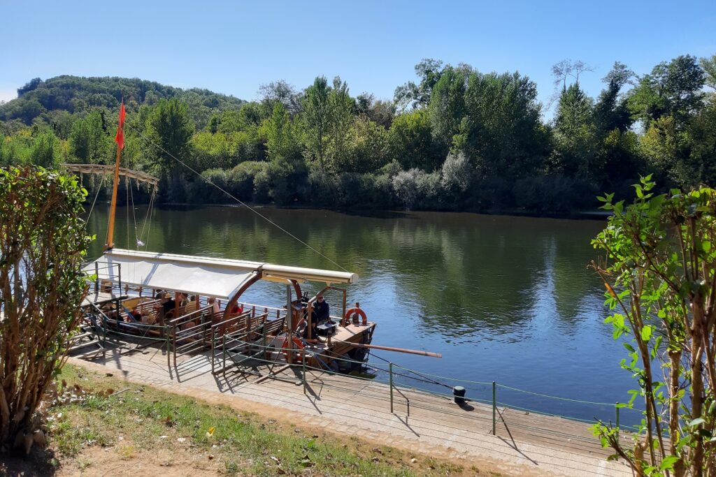 Paysage en Dordogne avec en fond des arbres et au premier plan un cours d'eau avec un bateau