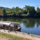 Paysage en Dordogne avec en fond des arbres et au premier plan un cours d'eau avec un bateau