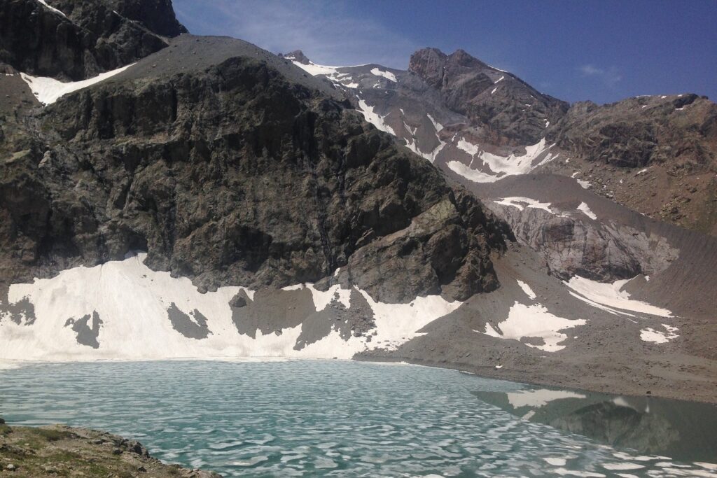 Paysage de montagne dans les écrins avec un lac de montagne en contre bas encadré par des sommets portant des restes de neige
