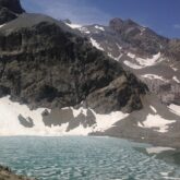 Paysage de montagne dans les écrins avec un lac de montagne en contre bas encadré par des sommets portant des restes de neige