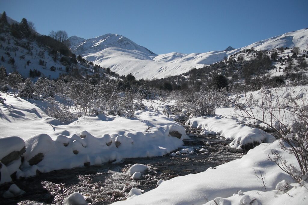 Paysage de montagne en bigarré avec un cours d'eau entouré de neige de part et d'autre et au fond des sommets