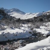 Paysage de montagne en bigarré avec un cours d'eau entouré de neige de part et d'autre et au fond des sommets