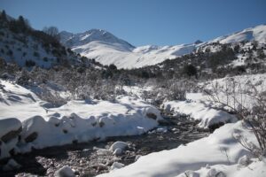 Paysage de montagne en bigarré avec un cours d'eau entouré de neige de part et d'autre et au fond des sommets