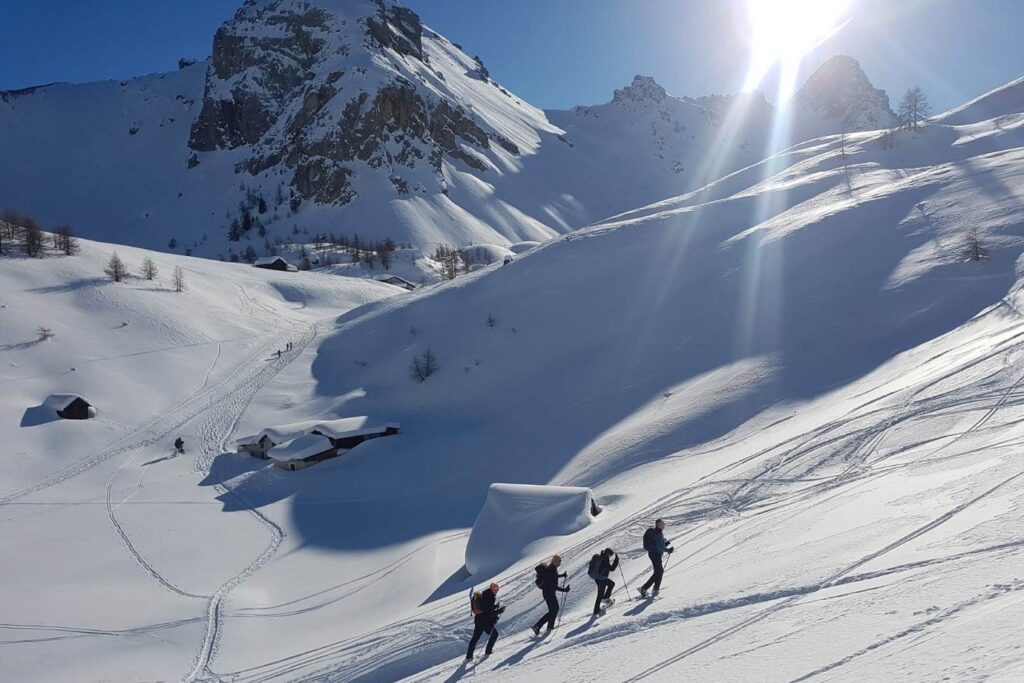 Groupe de randonneurs avec leur guide sur un sentier de randonnée dans le massif du Queyras sous un grand soleil en hiver lors d'un séjour de découverte de la zone en raquettes