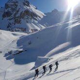 Groupe de randonneurs avec leur guide sur un sentier de randonnée dans le massif du Queyras sous un grand soleil en hiver lors d'un séjour de découverte de la zone en raquettes