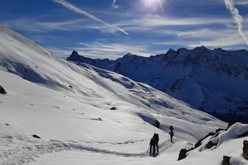 Paysage hivernal dans le Queyras avec un groupe de randonneurs sur un sentier en raquettes dans le massif du Queyras sous un grand soleil