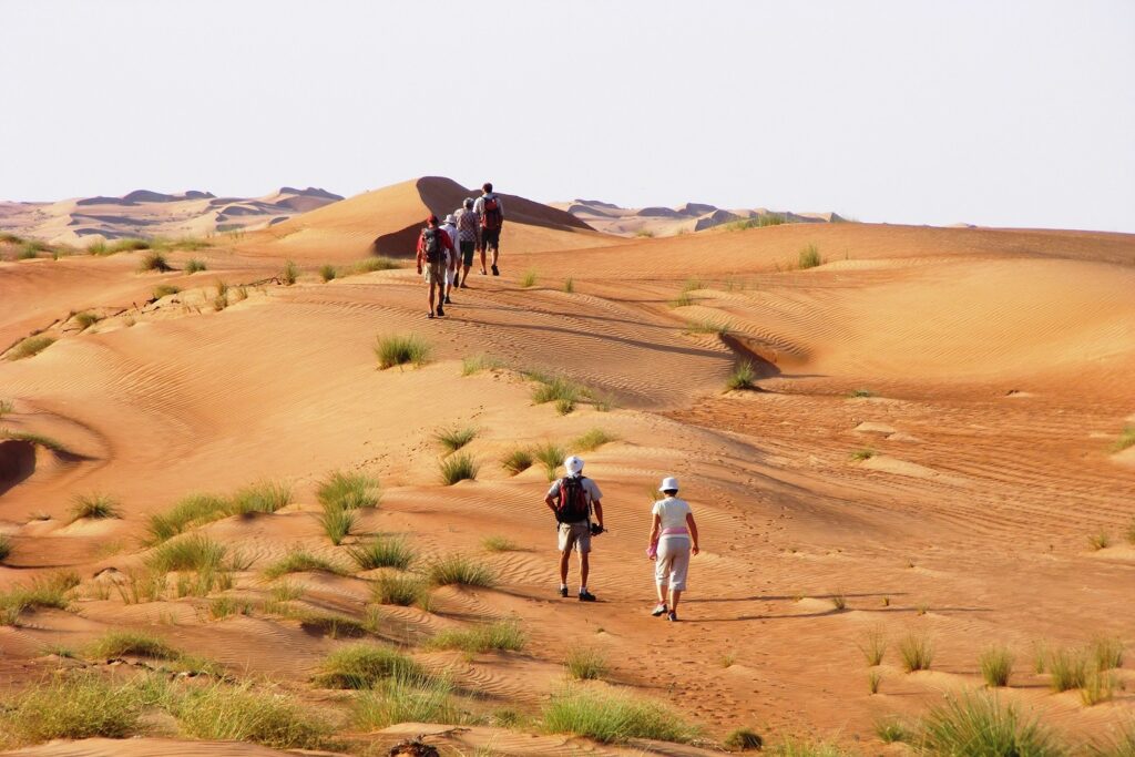 Groupe de randonneurs avec leur guide en train de marcher sur des dunes de sable à Oman