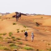 Groupe de randonneurs avec leur guide en train de marcher sur des dunes de sable à Oman
