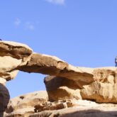 Groupe de randonneurs sur un sentier de randonnée avec une passerelle naturelle en pierre dans le désert du Wadi Rum en Jordanie