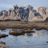 Paysage dans les Alpes avec des sommets aux couleurs grises en fond et un lac de montagne au premier plan