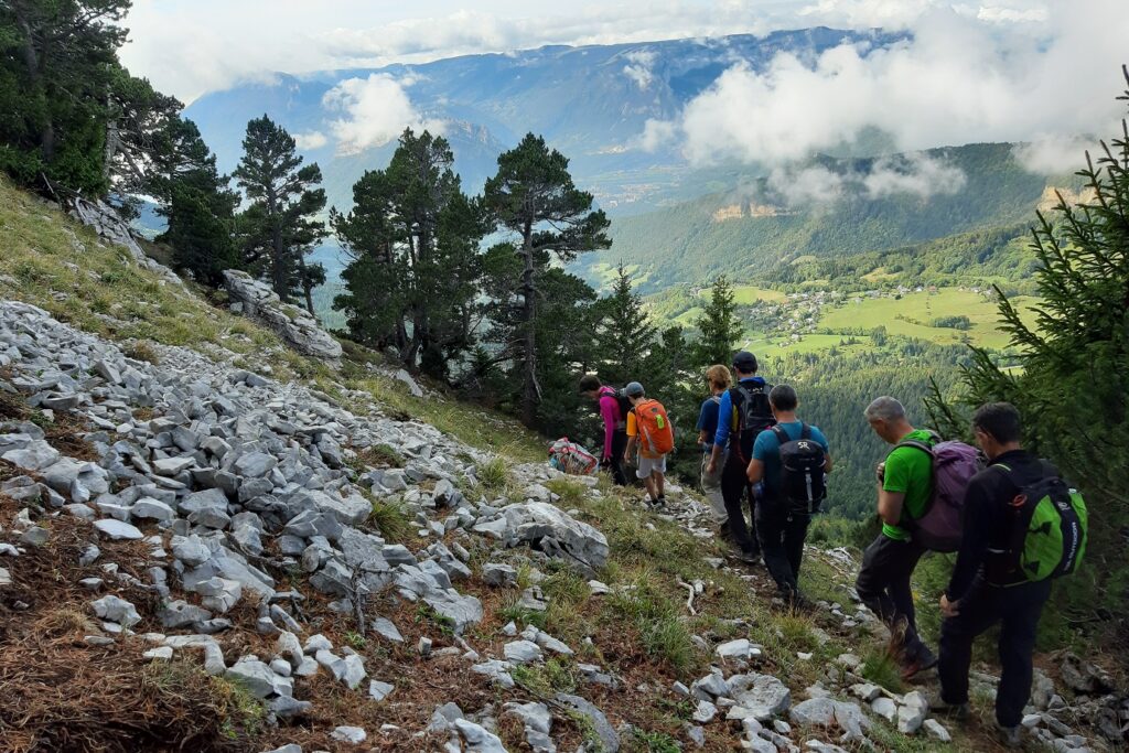 Groupe de randonneurs sur un sentier de randonnée avec une vallée en contrebas sur la droite et des rochers sur la gauche
