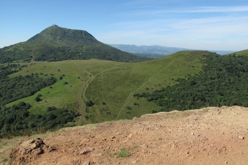 Paysage montagnard d'Auvergne avec des sommets et de l'herbe très verte sur les flancs de la montagne