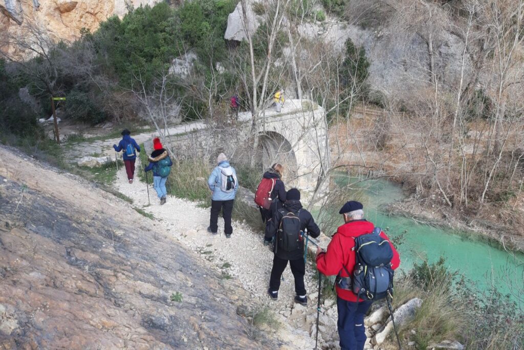 Groupe qui marche au bord de l'eau avec un pont en pierre devant eux