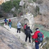 Groupe qui marche au bord de l'eau avec un pont en pierre devant eux