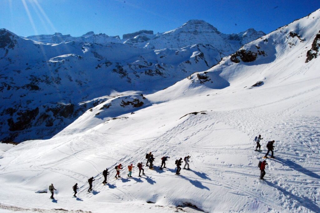 Groupe de randonneurs en raquettes en file indienne sur une pente enneigée, face aux sommets des Hautes-Pyrénées