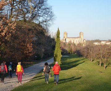 Gers-randonnee Randonneurs marchant sur un chemin en direction d'un village dans le Gers.