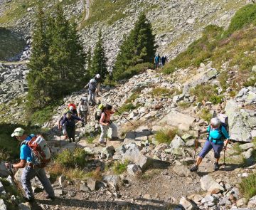 Groupe de randonneurs sur un sentier de randonnée avec beaucoup de cailloux en train de monter avec leur guide lors du tour du mont Blanc sud