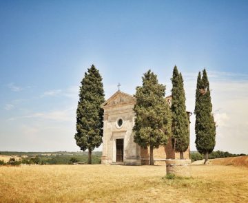 italie-toscane-sejour-randonnee Paysage toscan d'une abbaye encadré par deux cyprès, dans un environnement isolé et très sec, avec de l'herbe jaunie