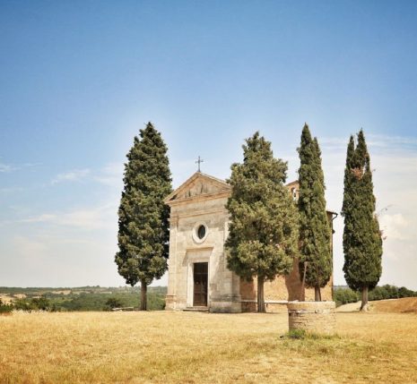 Paysage toscan d'une abbaye encadré par deux cyprès, dans un environnement isolé et très sec, avec de l'herbe jaunie