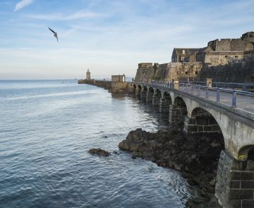 jersey-guernesey-randonnee-sejour Paysage jersey, une des îles au large de la Bretagne avec un pont sur la droite et des habitations et l'océan sur la gauche