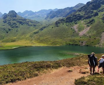 Paysage de montagne avec un sentier sur lequel un groupe de marcheurs avance et un lac sur la gauche