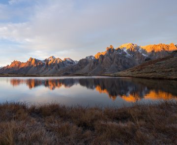 Paysage de montagne avec un lac au centre de l'image et des sommets en fond, avec le début du levé du soleil qui touche les sommets
