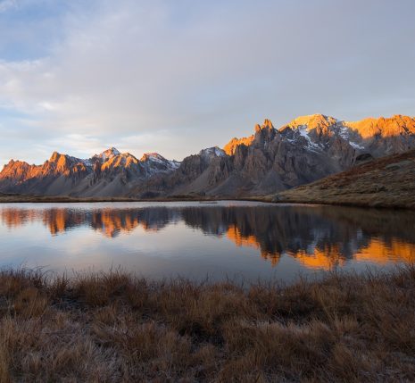 Paysage de montagne avec un lac au centre de l'image et des sommets en fond, avec le début du levé du soleil qui touche les sommets