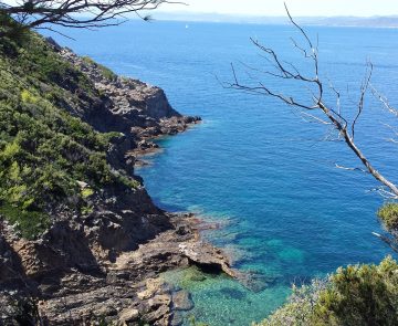Paysage de littoral avec de l'eau turquoise en contrebas et des rochers de part et d'autre d'une petite crique