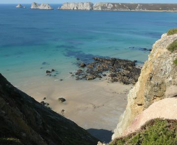 ouessant-randonnee Paysage côtier avec l'eau turquoise sur une plage de sable surplombée par des rochers