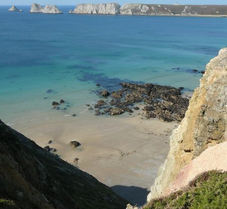 Paysage côtier avec l'eau turquoise sur une plage de sable surplombée par des rochers