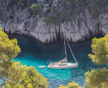 Prise de vue en hauteur de l'eau turquoise avec un bateau, encadré de falaises et d'arbres