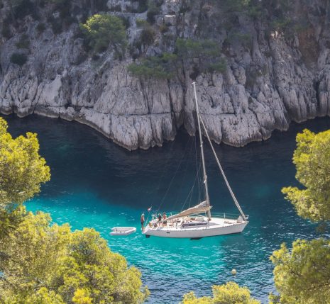 Prise de vue en hauteur de l'eau turquoise avec un bateau, encadré de falaises et d'arbres