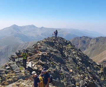 Groupe de randonneurs au sommet d'une montagne, face à un paysage montagnard où l'on voit des sommets à l'horizon.