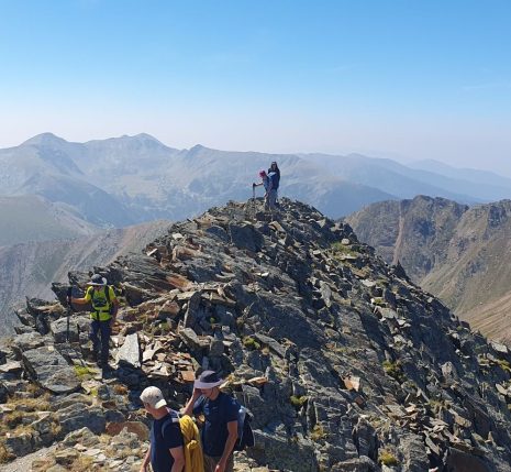 Groupe de randonneurs au sommet d'une montagne, face à un paysage montagnard où l'on voit des sommets à l'horizon.