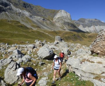 Groupe de randonneurs montant à flanc d'une montagne entre les roches avec différents sommets derrière