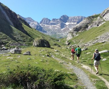 Groupe de randonneurs sur un sentier entre Gavarne et Cauterets encadré par des sommets, un temps estival ainsi que de la végétation variée