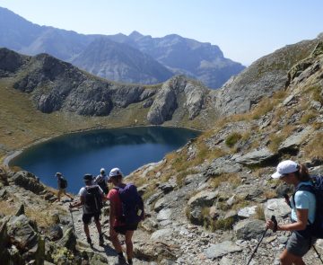 Groupe de randonneurs sur un sentier avec leur guide se dirigeant vers un lac de montagne entouré de sommets