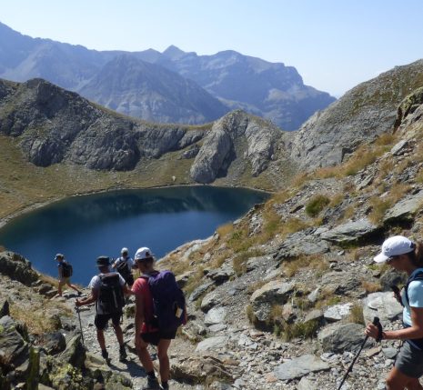 Groupe de randonneurs sur un sentier avec leur guide se dirigeant vers un lac de montagne entouré de sommets