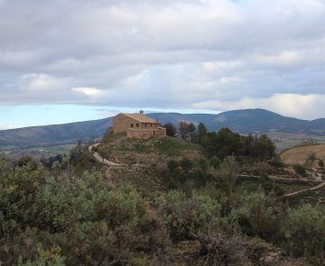Paysage de montagne avec une habitation au sommet d'une colline encadrée d'arbres et de végétation, dans la zone de Pampelune en Navarre