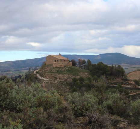 Paysage de montagne avec une habitation au sommet d'une colline encadrée d'arbres et de végétation, dans la zone de Pampelune en Navarre