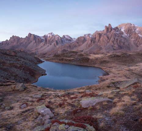Paysage de montagne dans la vallée de l'Ubaye avec un ciel et une lumière rosée due au coucher ou lever du soleil, avec un lac en contrebas