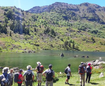 Groupe de randonneurs avec leur guide face à un lac de montagne et des sommets qui leur font face