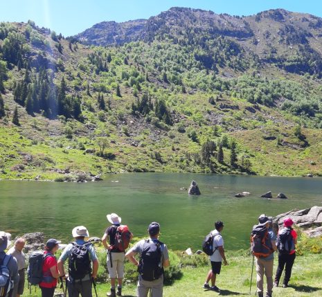 Groupe de randonneurs avec leur guide face à un lac de montagne et des sommets qui leur font face